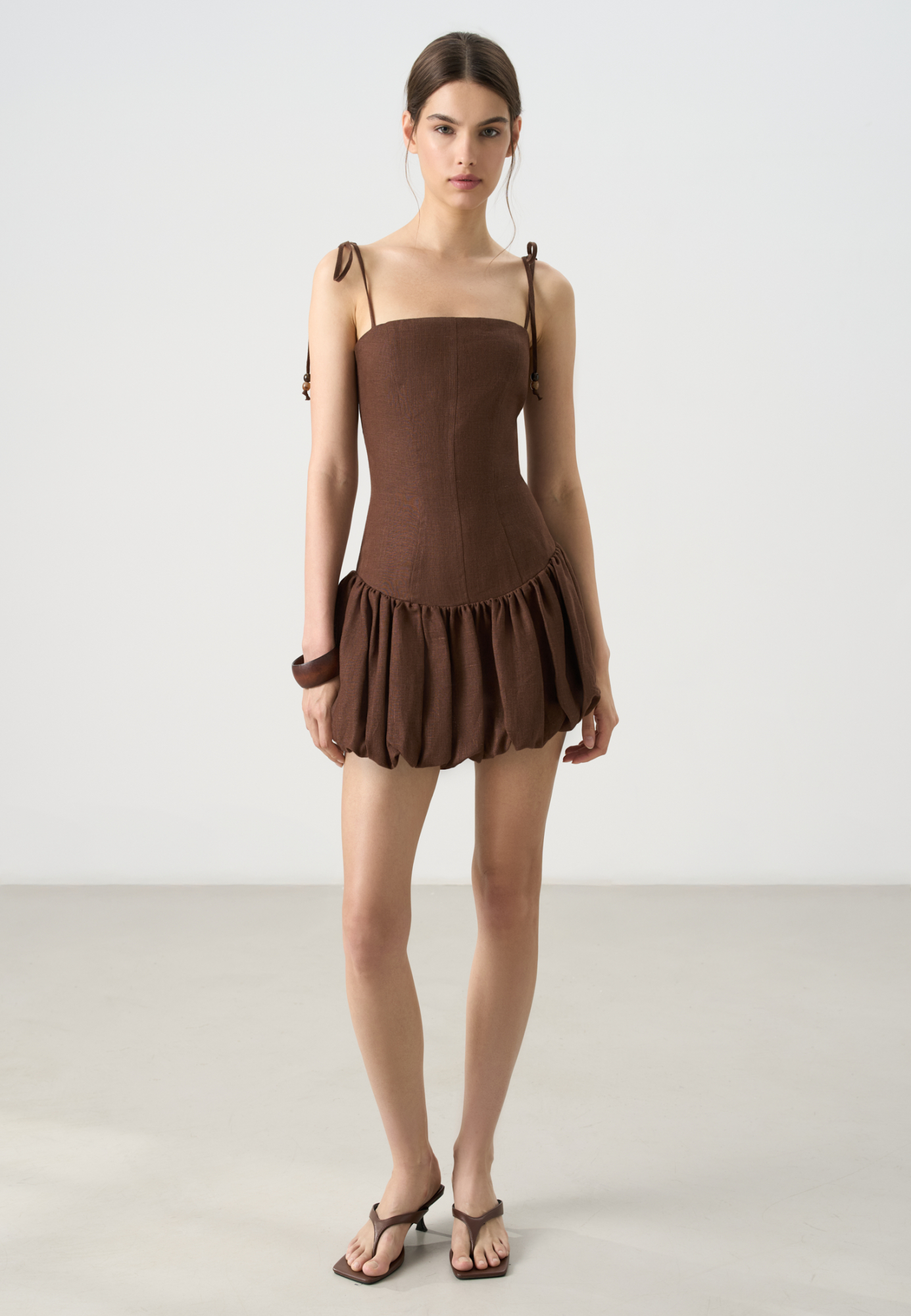 Платье длины мини из 100% льна с юбкой-баллон. Модель приталенного силуэта, с корсетным верхом, на тонких бретельках, декорированных крупными бусинами. Спинка изделия выполнена на резинке. 
