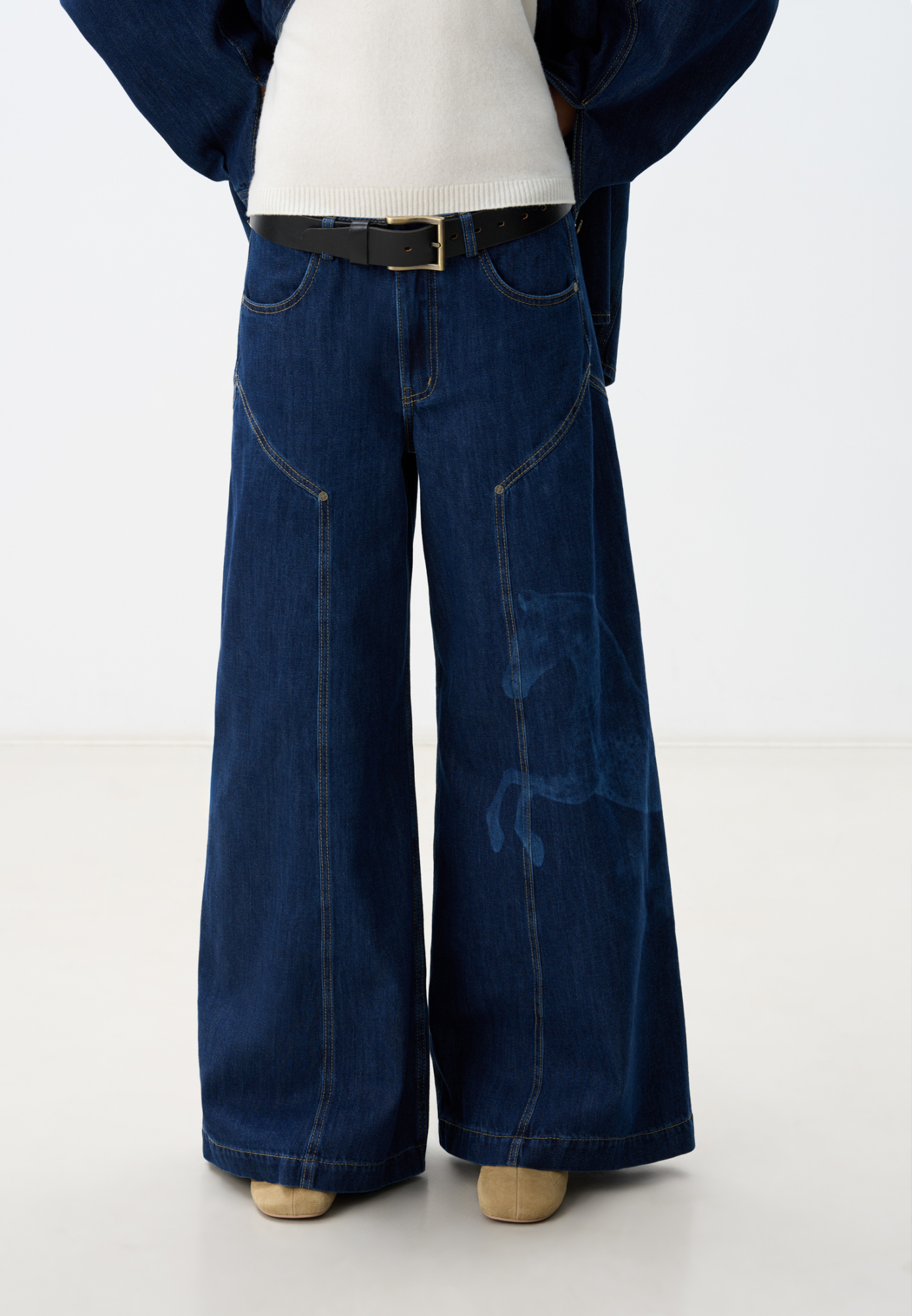 Широкие джинсы из 100% хлопка с принтом лошадей. Модель на средней посадке, с пятью карманами и шлевками на поясе для ремня. Застежка на молнию и пуговицу. На штанинах изделие декорировано принтом лошадей, выполненным лазером, и объемными геометрическими вытачками с заклепками. <br />
Модель в стиле дерби - направления в моде, которое имитирует одежду для скачек.