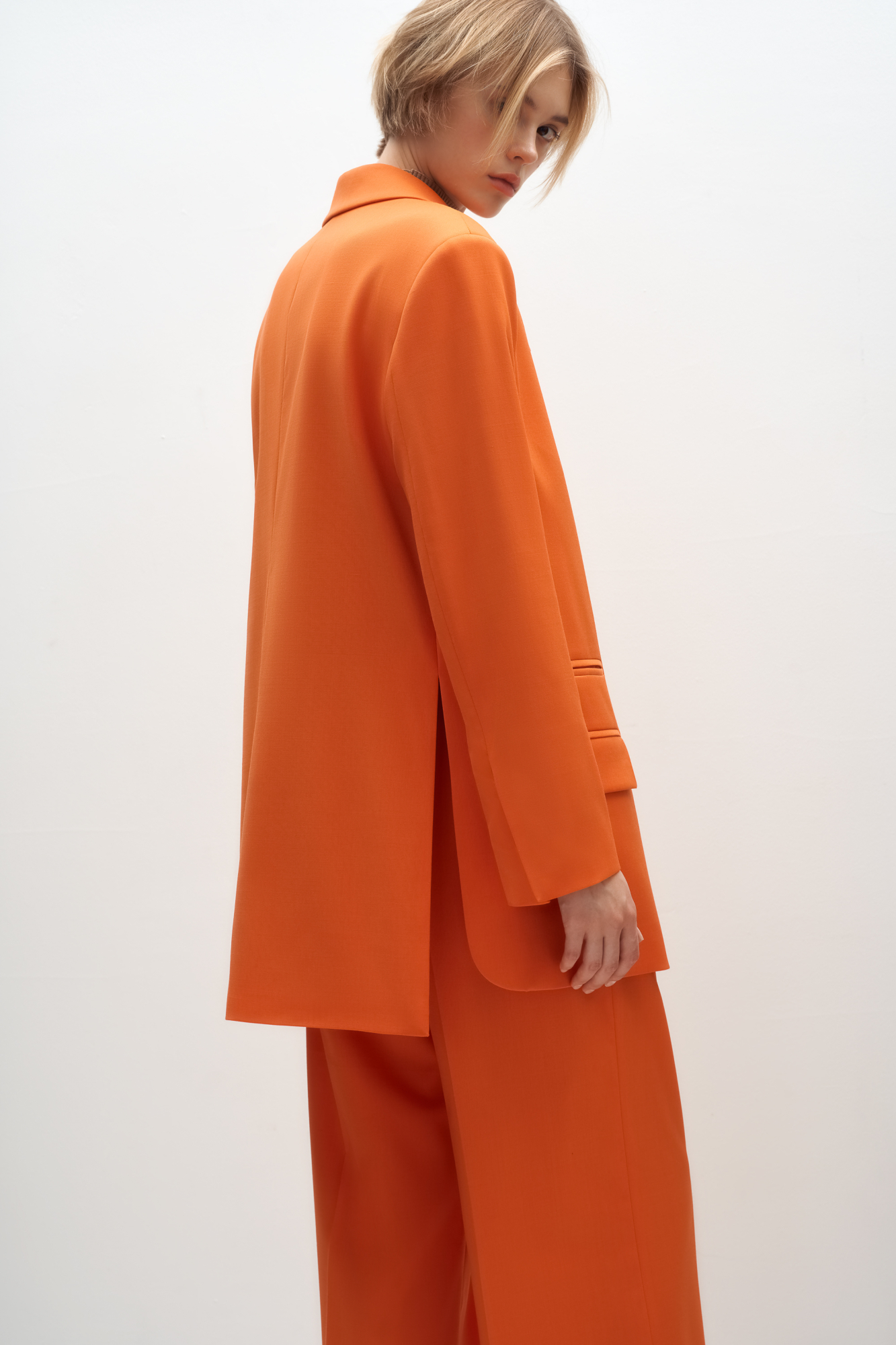 Классический костюм, состоящий из однобортного жакета и брюк палаццо. Жакет прямого кроя судлиненной спинкой, лацканами и двумя прорезными карманами с клапанами. Брюки прямого кроя с боковыми карманами и застежкой на молнию.