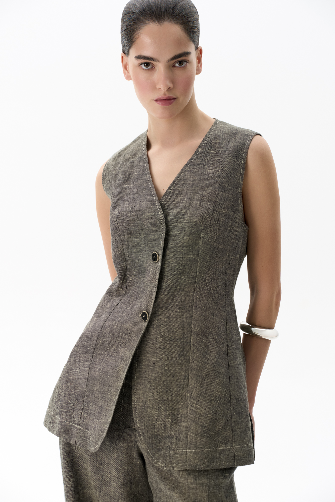 Удлиненный жилет из 100% льна. Модель приталенного силуэта, с V-образным вырезом горловины, вертикальными вытачками, ремнем на спинке и разрезами по бокам. Изделие бех подкладки.