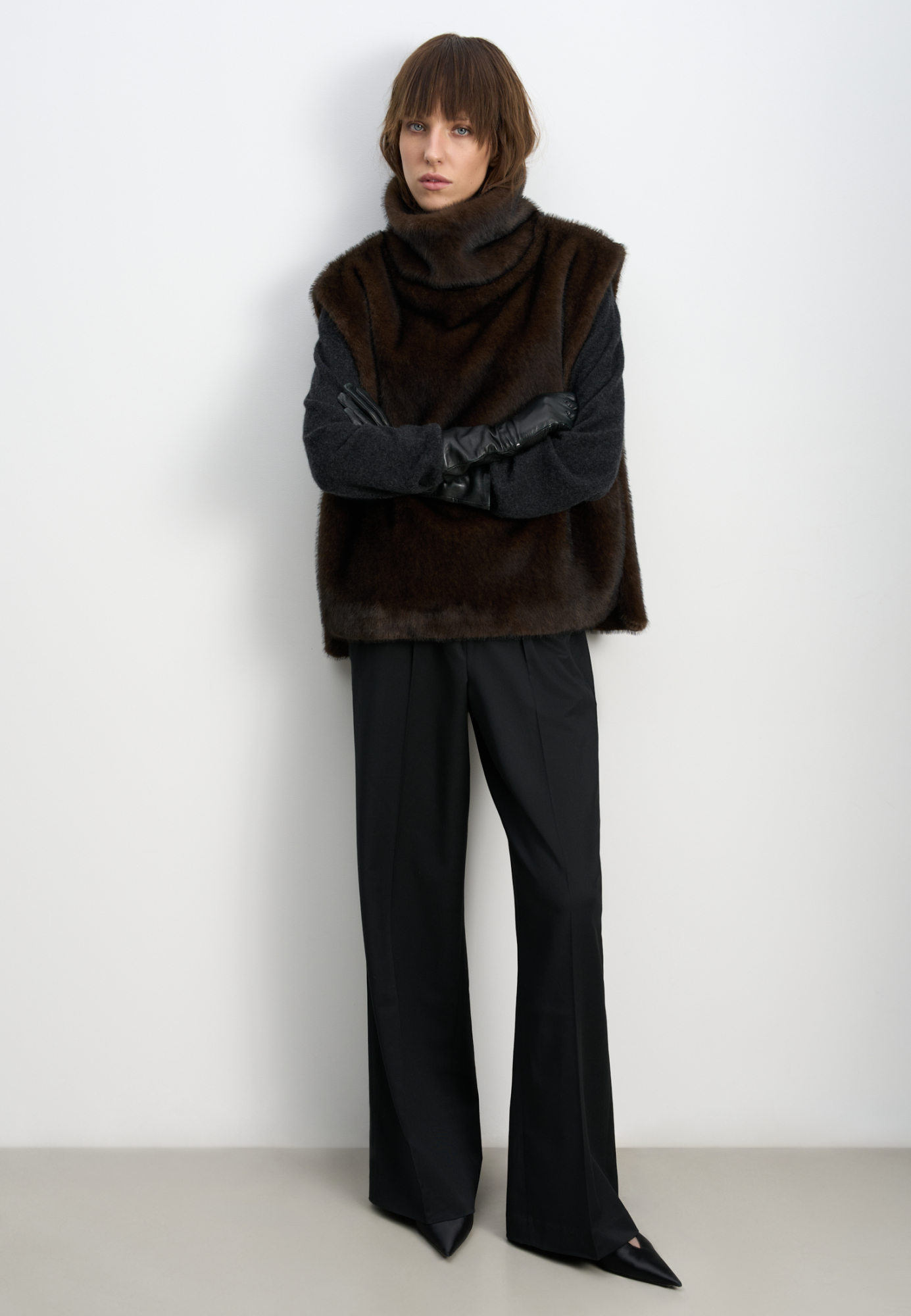 Жилет из экомеха с воротником-стойкой и карманом-кенгуру. Модель фиксируется по бокам на кнопки. Изделие выполнено на подкладке.