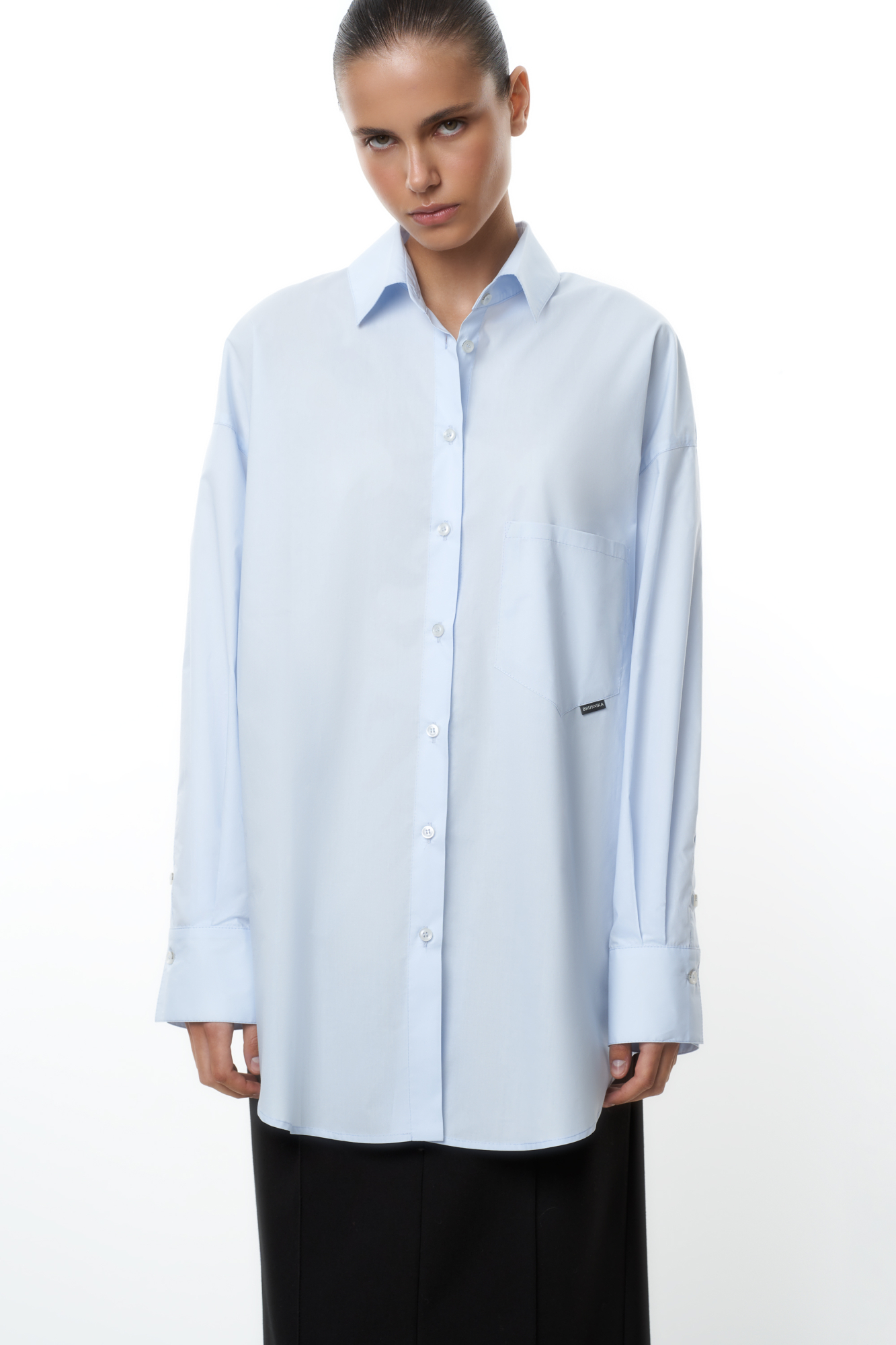 Рубашка с накладным карманом и брендированным ярлыком. Модель свободного силуэта, длинные рукава с манжетами и асимметричный нижний край.