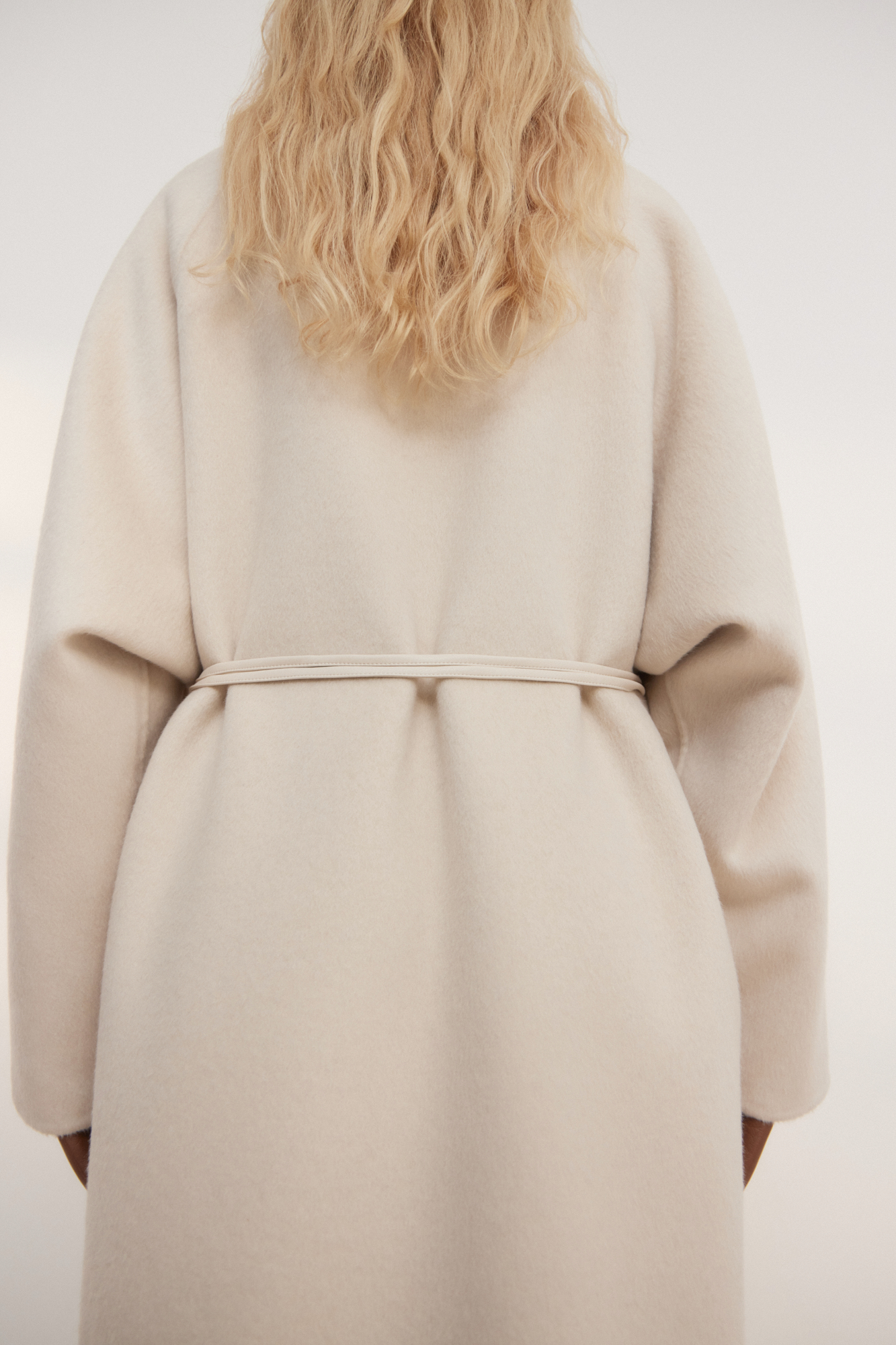 Шерстяное пальто из двусторонней ткани. Модель прямого кроя без воротника. Застежка на скрытые магнитные пуговицы. Изделие без подкладки. Модель декорирована асимметричным лацканом. Пояс из экокожи в комплекте.