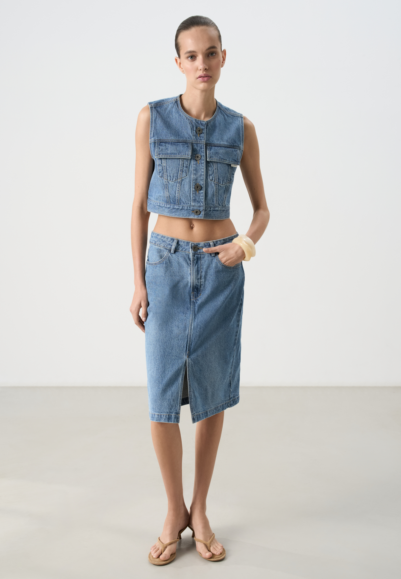 Джинсовая юбка длины миди из 100% хлопка. Модель по фигуре, с карманами, шлевками на поясе для ремня и невысоким разрезом спереди. Застежка на молнию и пуговицу.