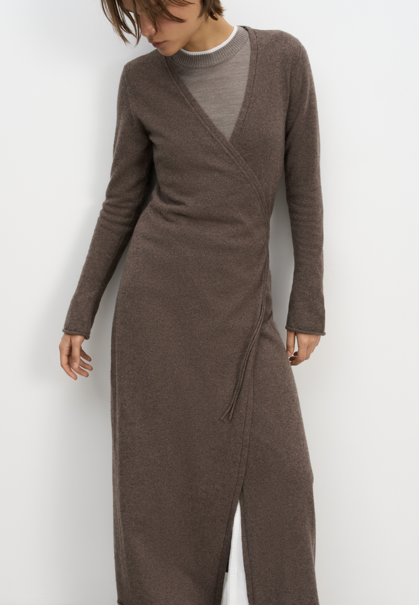 Трикотажное платье на запах из шерсти и кашемира. Модель приталенного силуэта с V-образным вырезом, длинными рукавами и кулиской на талии. Подол платья и манжеты рукавов декорированы валиками.