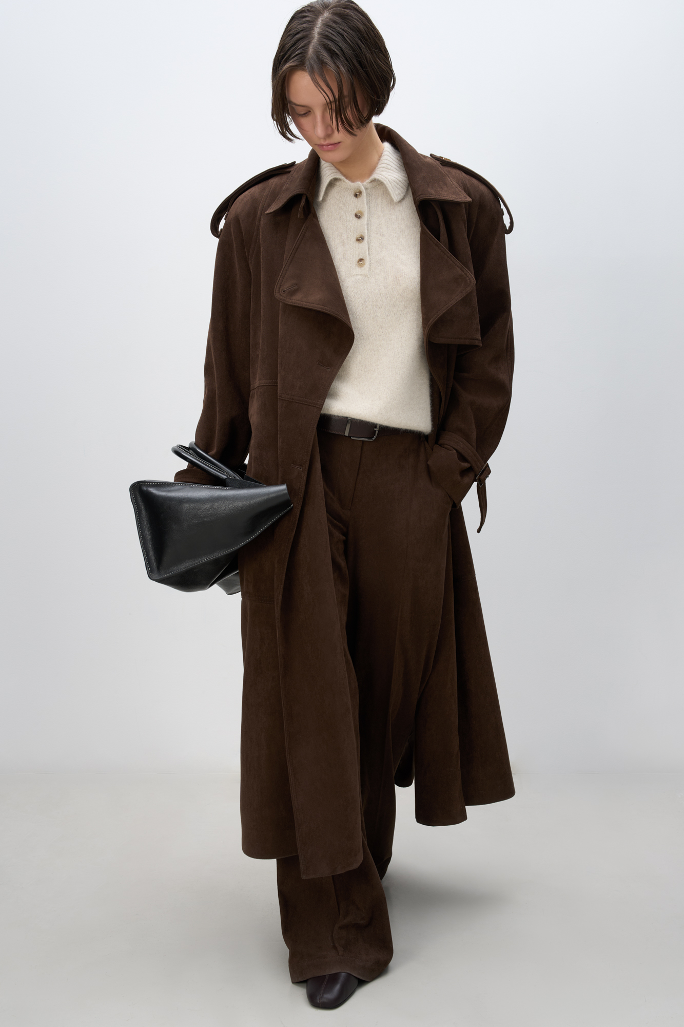 Двубортный длинный тренч, выполненный из ткани с имитацией внешнего вида и свойств натуральной замши. <br />
Модель с отложным воротником, отлетной кокеткой, патами на плечах и манжетах рукавов, карманами и шлевками на талии для ремня. Изделие выполнено на подкладке.