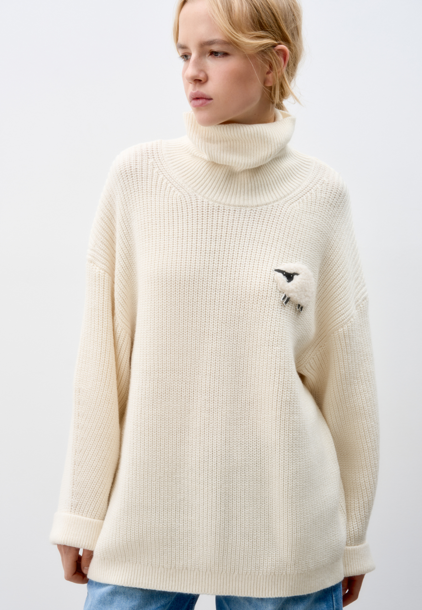 Трикотажный джемпер из шерсти альпака. Модель свободного силуэта, с высоким вывязанным горлом, спущенной линией плеч и длинными рукавами с манжетами. Изделие декорировано объемным элементом в виде барашка. 