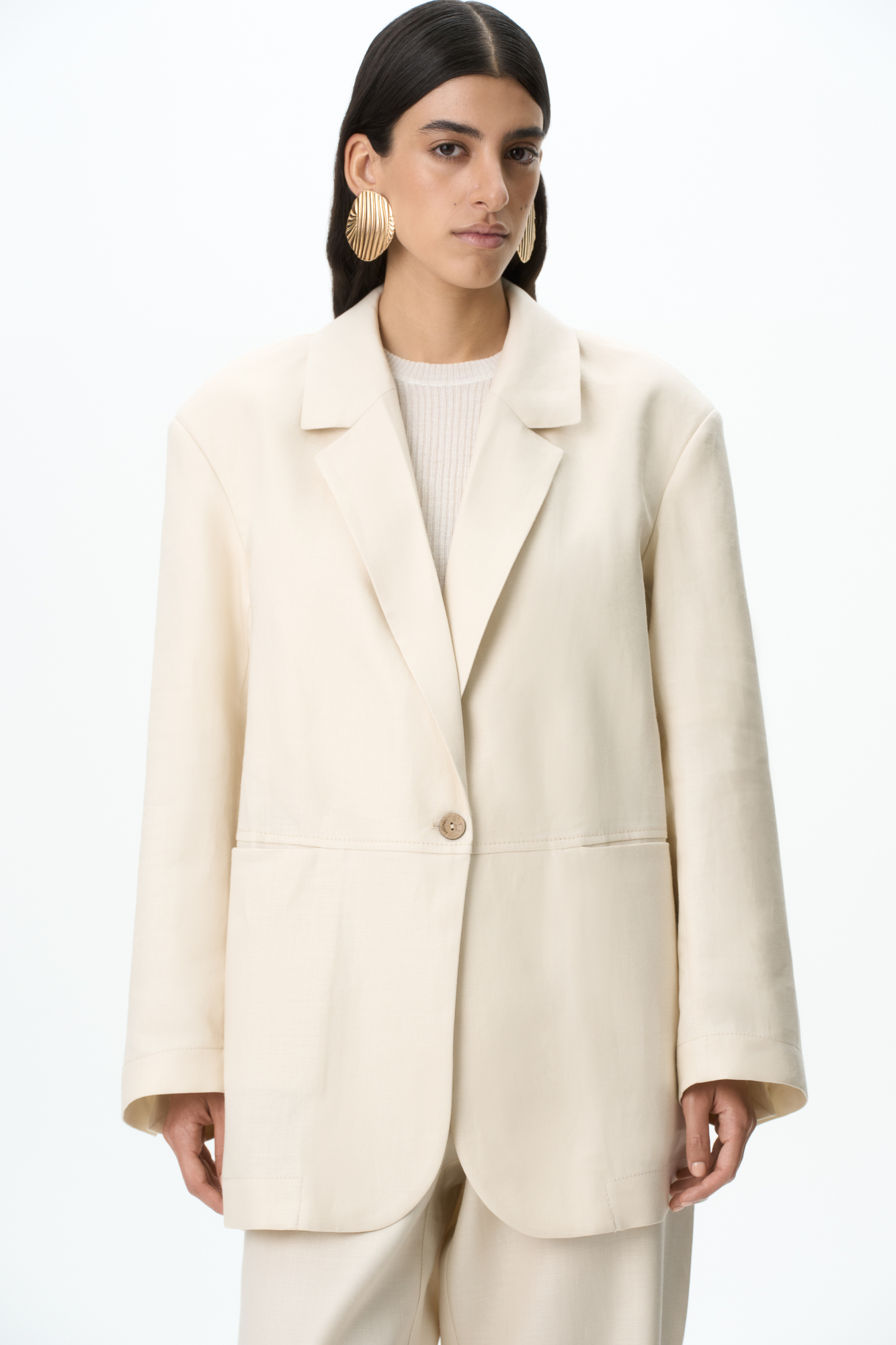 Однобортный жакет из 100% льна. Модель свободного силуэта с прорезными карманами спереди. Застежка на пуговицу. Разрезы на пуговицах на рукавах. Дополнить образ можно брюками в таком же стиле.