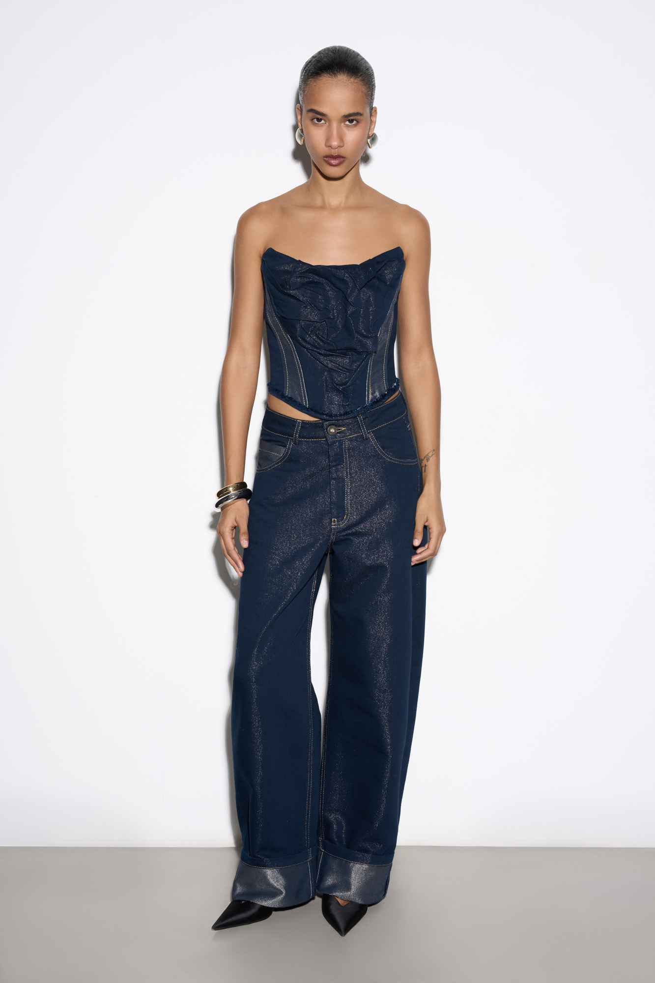 Джинсы relaxed fit из хлопка с добавлением металлизированной нити. Модель с пятью карманами, шлевками на поясе для ремня и застежкой на молнию и кнопку. Изделие декорировано высокими подворотами. 