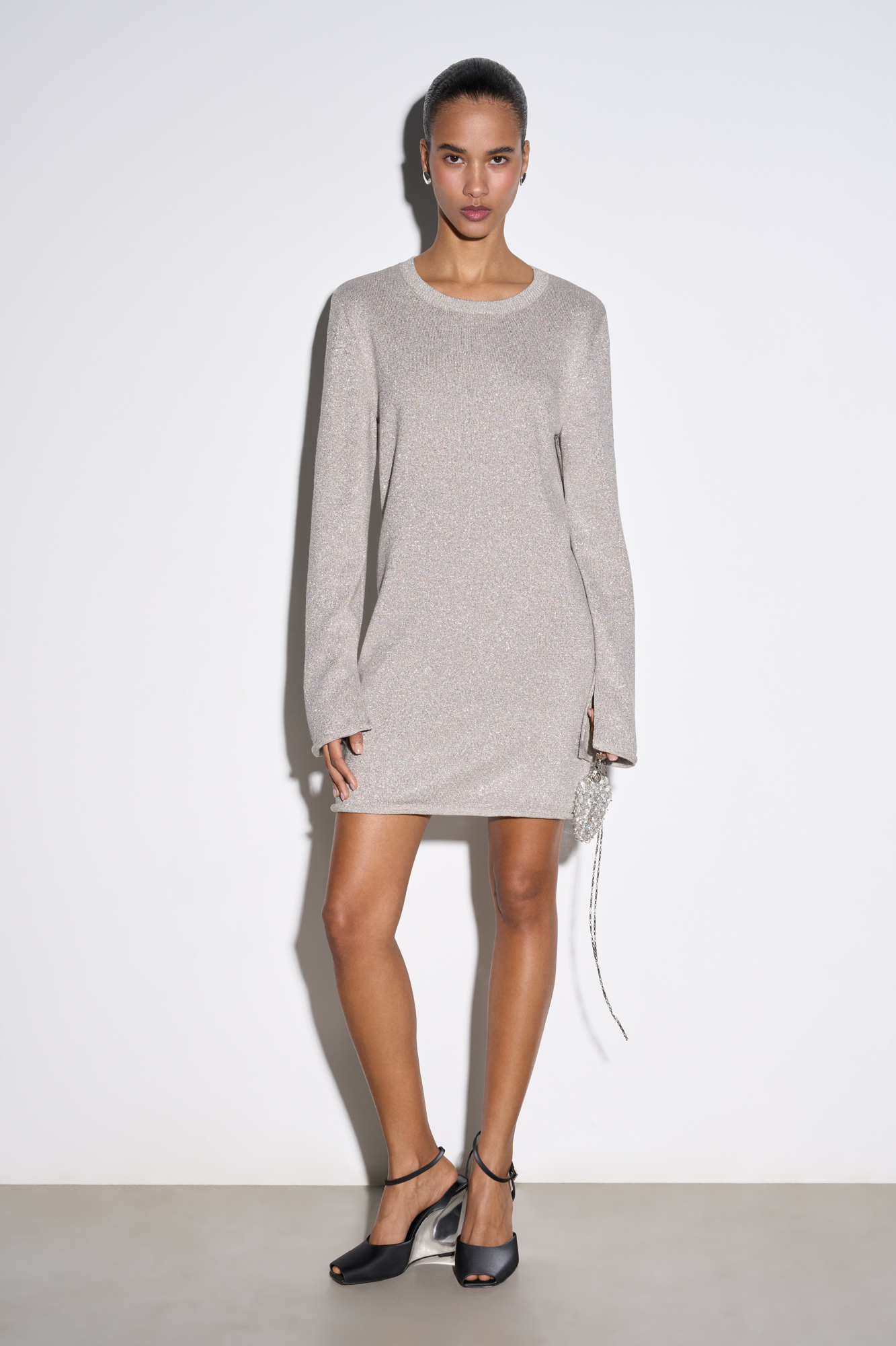 Трикотажное платье длины мини из вискозы с добавлением люрекса. Модель свободного силуэта с круглой горловиной и длинными рукавами. Края изделия декорированы валиком.