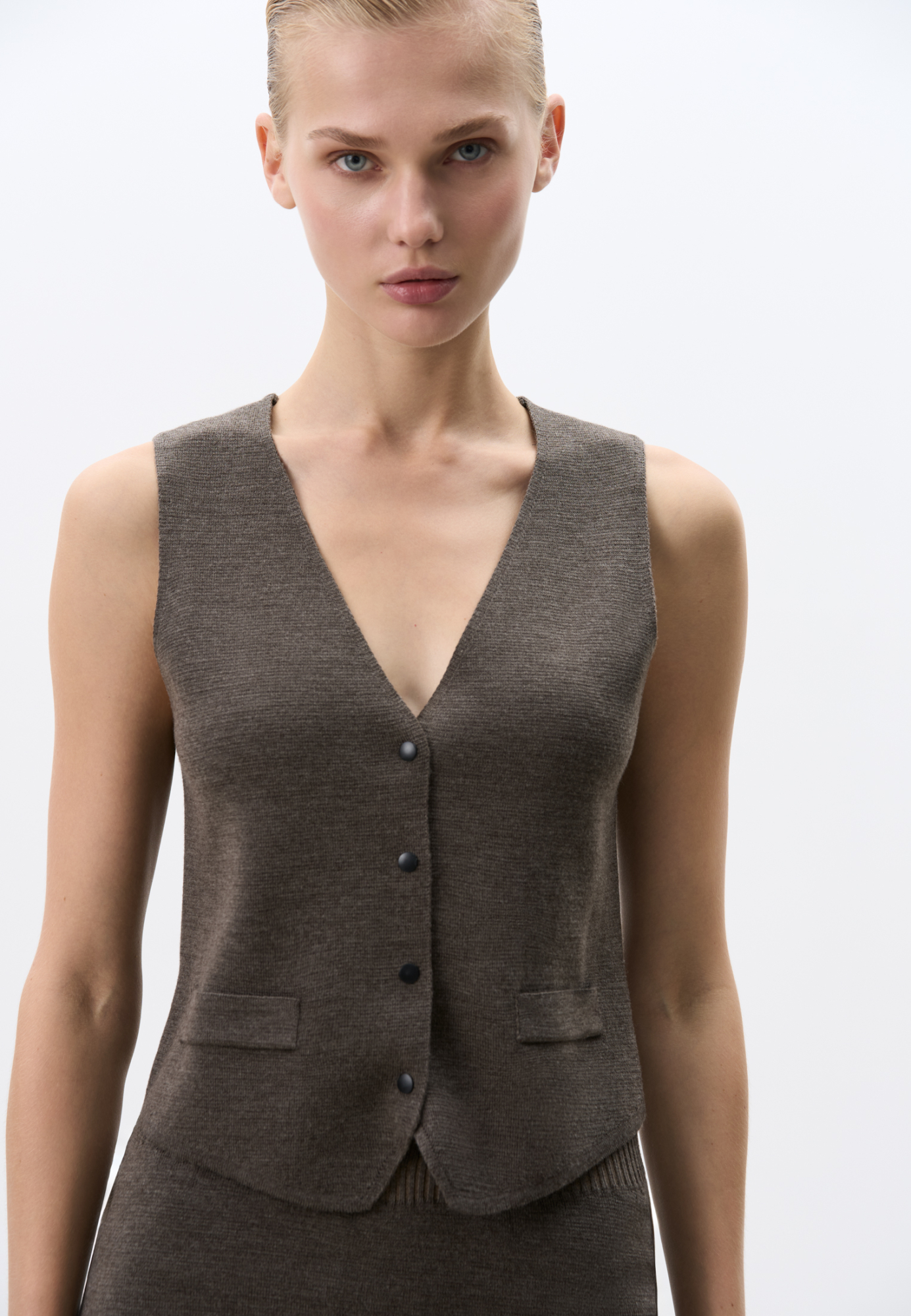 Трикотажный однобортный жилет из шерсти мериноса экстрафайн. Модель прямого кроя с имитацией карманов с клапанами и V-образным вырезом. Застежка на кнопки. Изделие без подкладки. Дополнить образ можно жакетом, бомбером, брюками или юбкой.