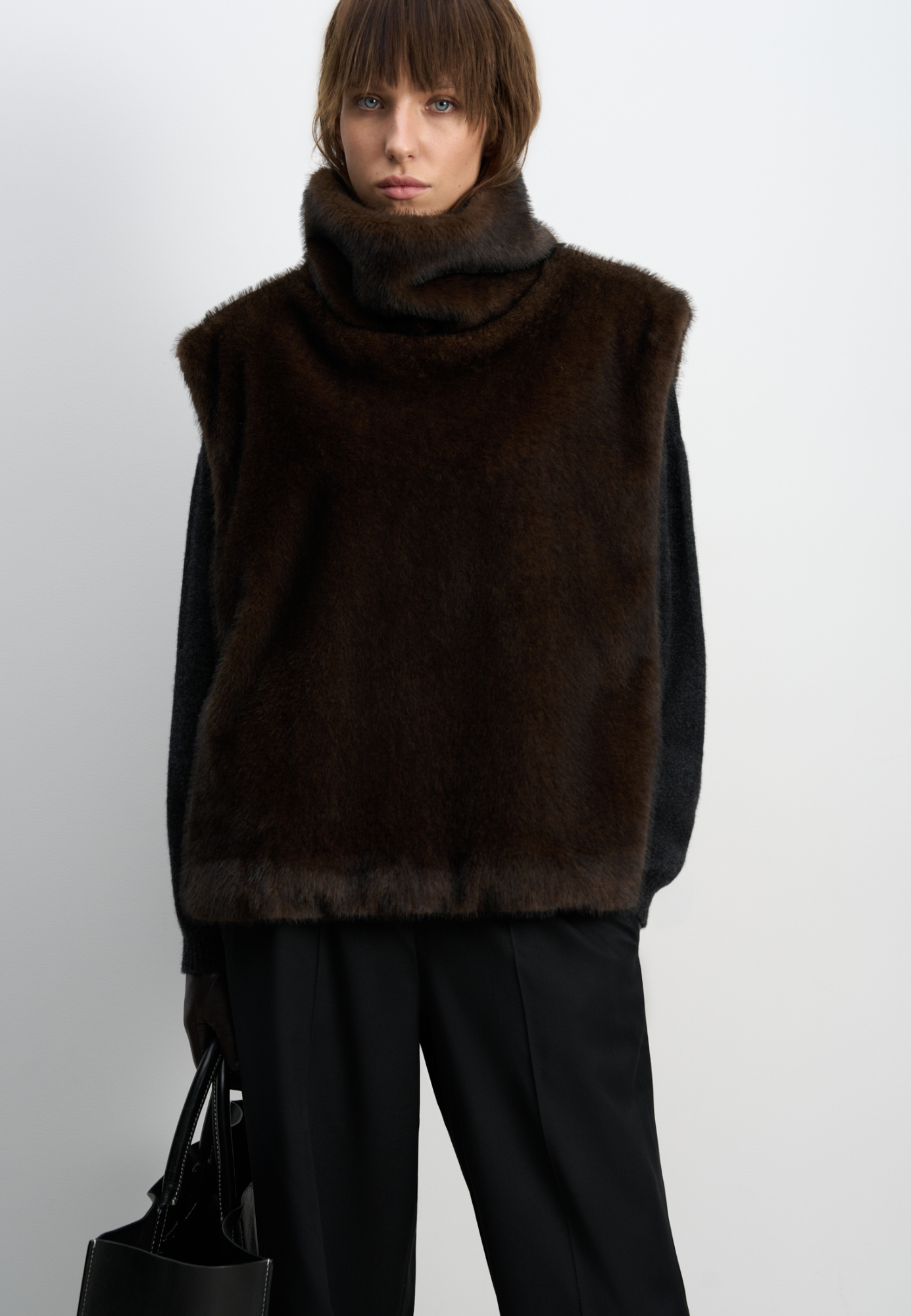 Жилет из экомеха с воротником-стойкой и карманом-кенгуру. Модель фиксируется по бокам на кнопки. Изделие выполнено на подкладке.