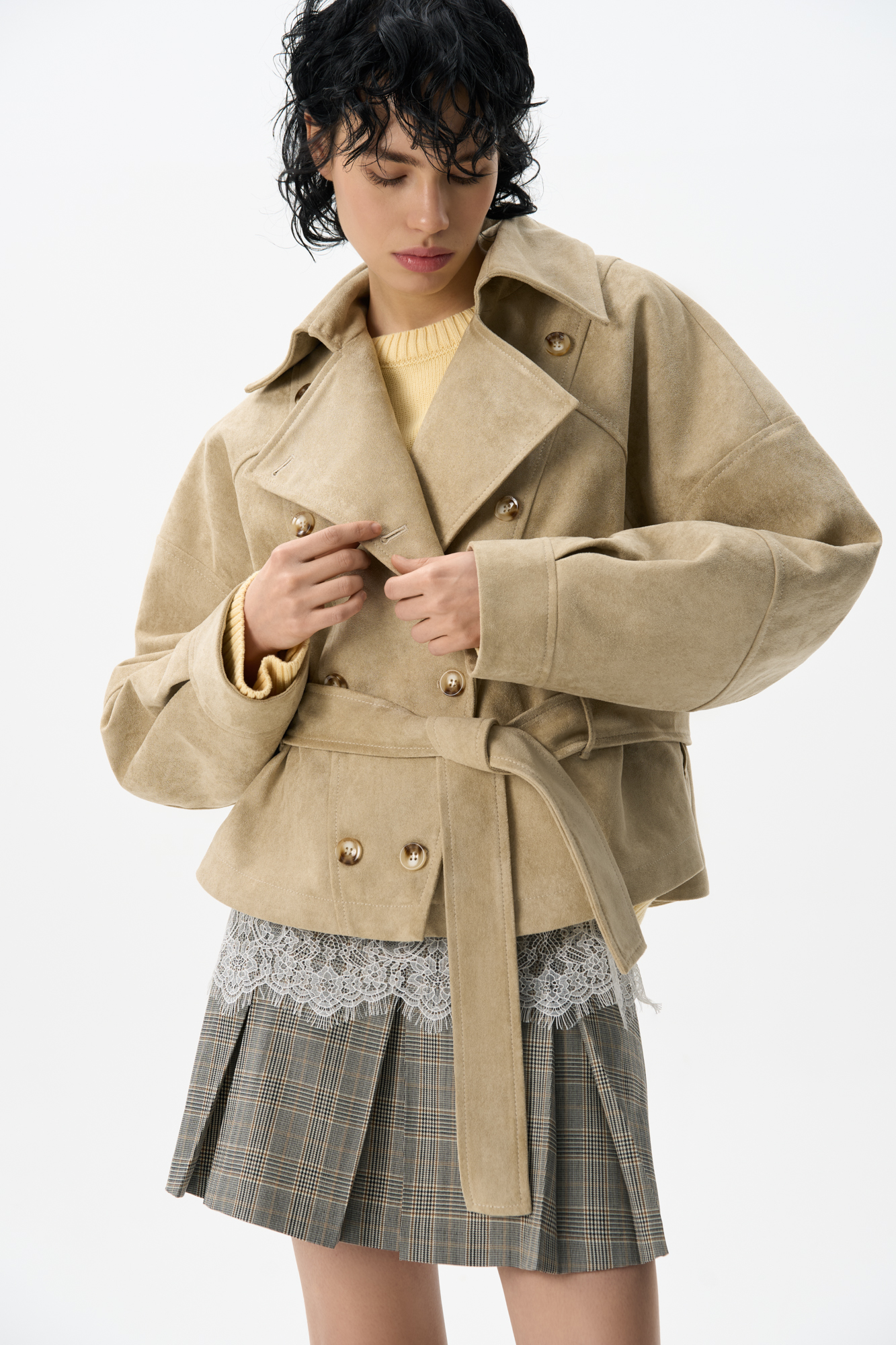 Двубортный короткий тренч сложной геометрии, выполненный из ткани с имитацией внешнего вида и свойств натуральной замши. Модель с отложным воротником, свободными рукавами со спущенной линией плеч, шлевками на поясе и ремнем.
