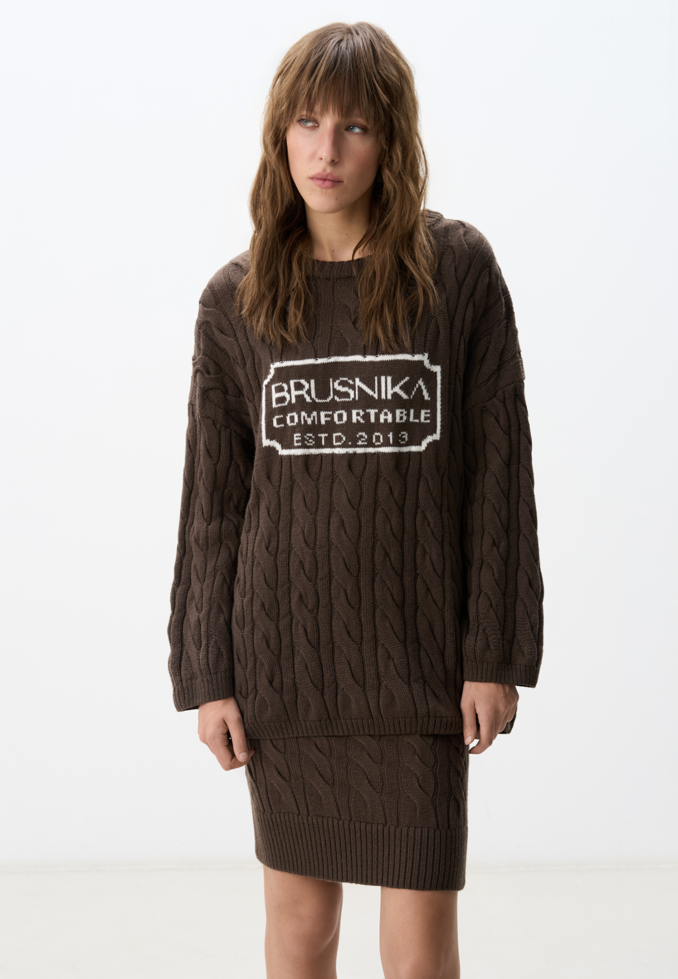 Трикотажный джемпер с объемными косами из мягкой шерсти. Модель свободного силуэта, со спущенной линией плеч и круглым вырезом. Изделие декорировано брендированным жаккардом на груди. Дополнить образ можно брюками и юбкой в том же стиле.