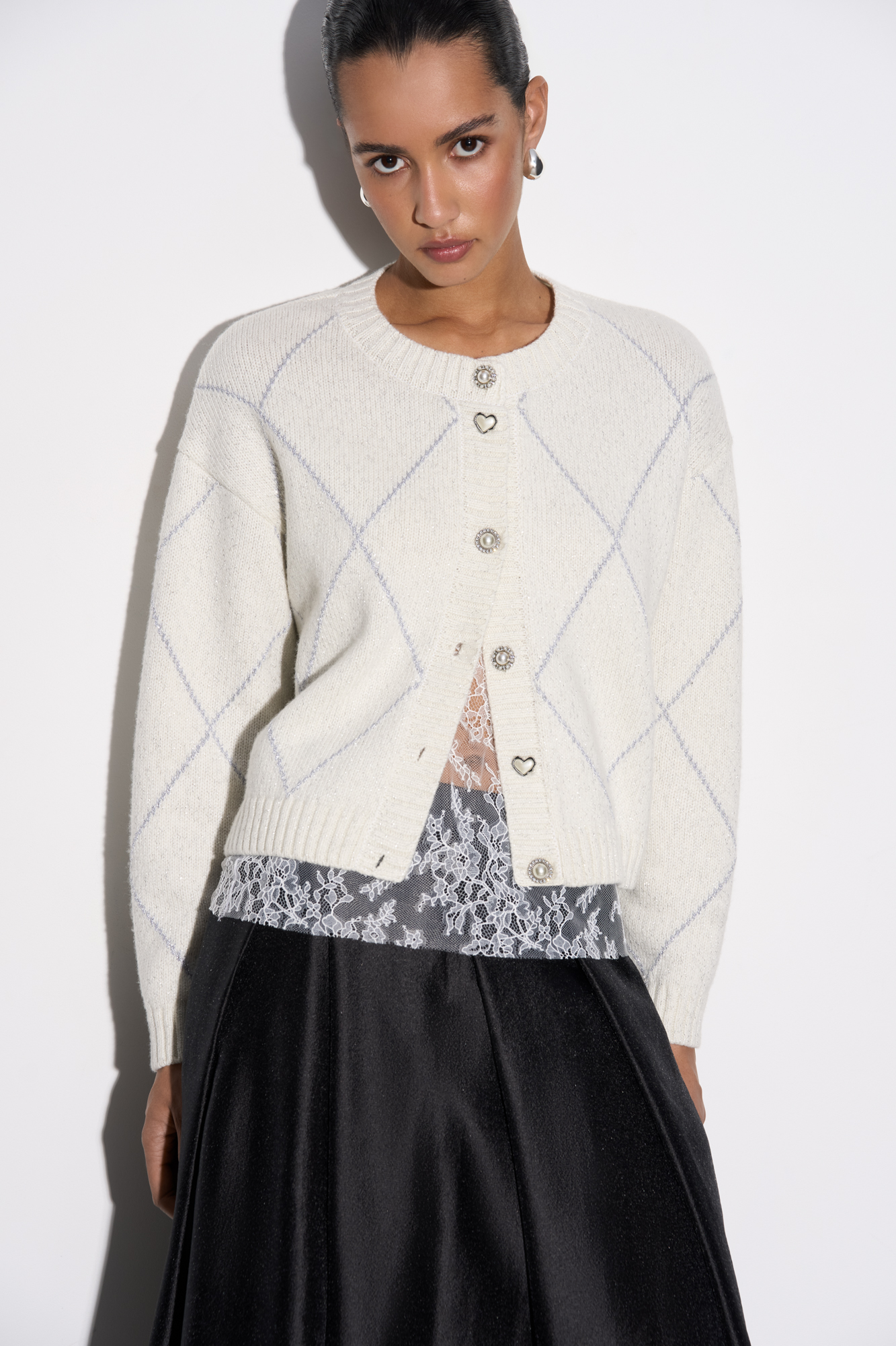 Трикотажный кардиган с узором аргайл из шерсти яка с добавлением люрекса. Модель свободного силуэта со спущенной линией плеч, круглым вырезом горловины и застежкой на крупные пуговицы. Края изделия выполнены в рубчик.