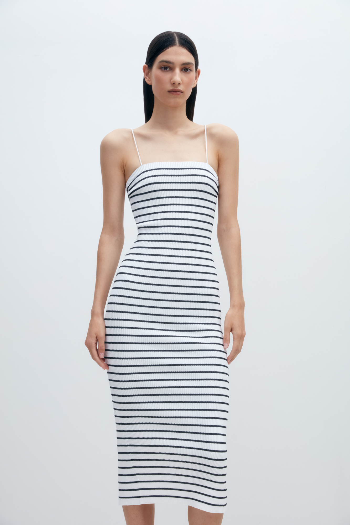 Трикотажное платье длины миди из вискозы в рубчик. Модель приталенного силуэта, на тонких бретельках и разрезом сзади.
