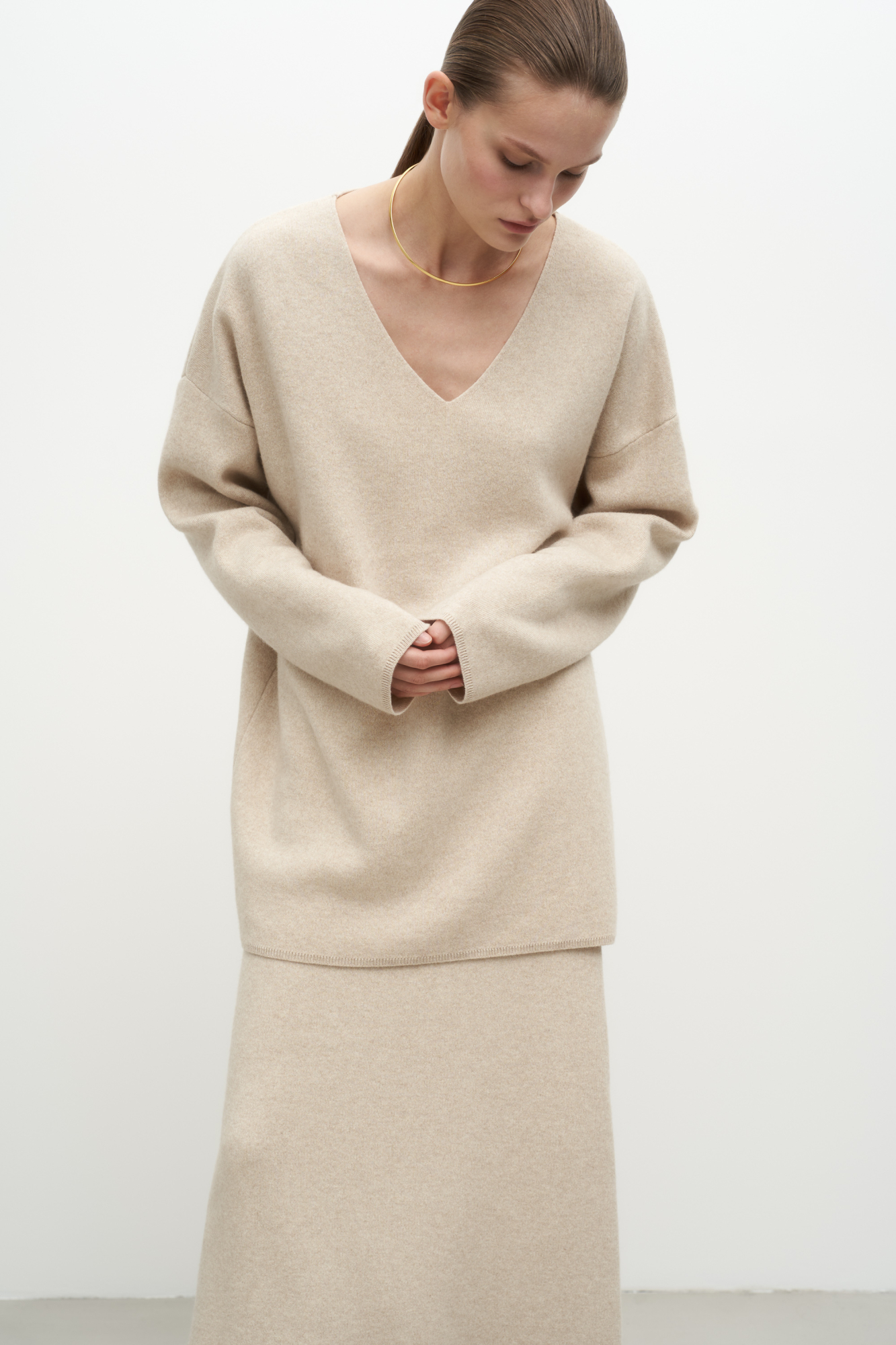 Удлиненный трикотажный джемпер из шерсти с добавлением кашемира. Модель свободного силуэта со спущенной линией плеча и глубоким V-образным вырезом. Дополнить образ можно комплектной юбкой.