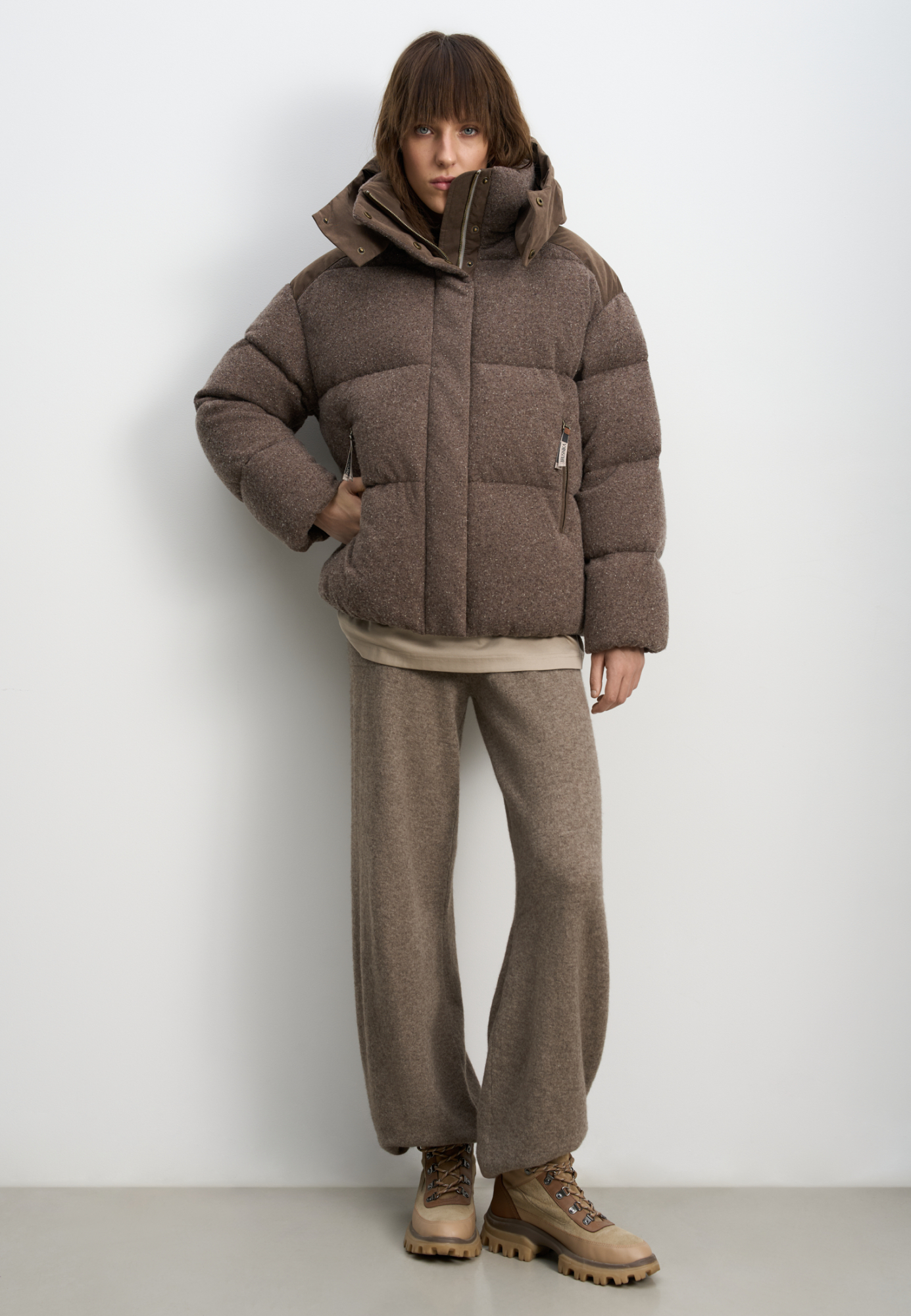 Трикотажный пуховик из шерсти с добавлением вискозы и шелка. Модель свободного силуэта с воротником-стойкой, капюшоном и карманами на молниях. Застежка на молнию под планкой с кнопками. 