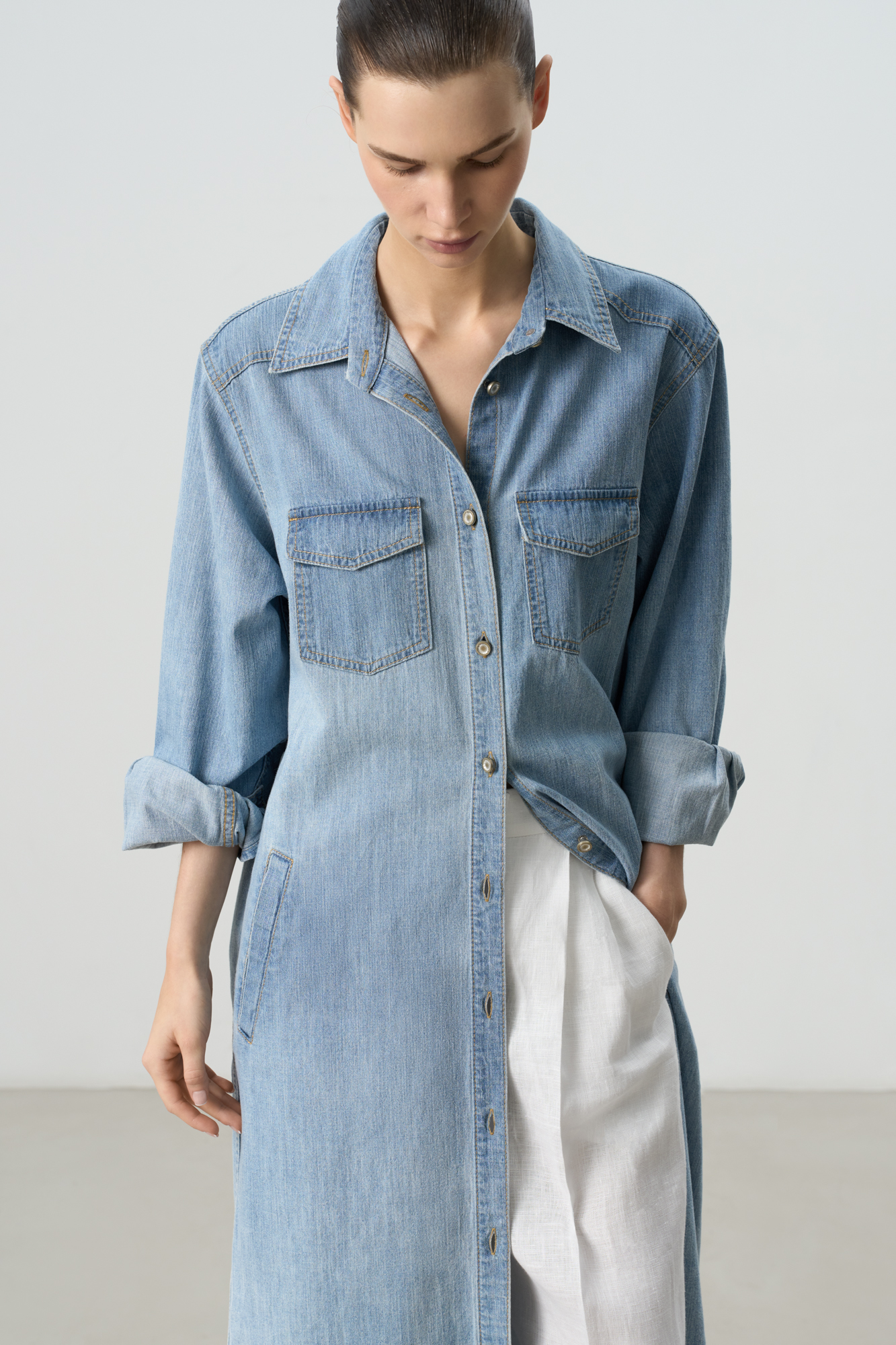 Джинсовое платье-рубашка длины миди из 100% хлопка. Модель прямого силуэта с длинными рукавами с манжетами на пуговицах, отложным воротником, двумя накладными карманами с клапанами на груди и двумя боковыми карманами. Застежка на пуговицы по вей длине.