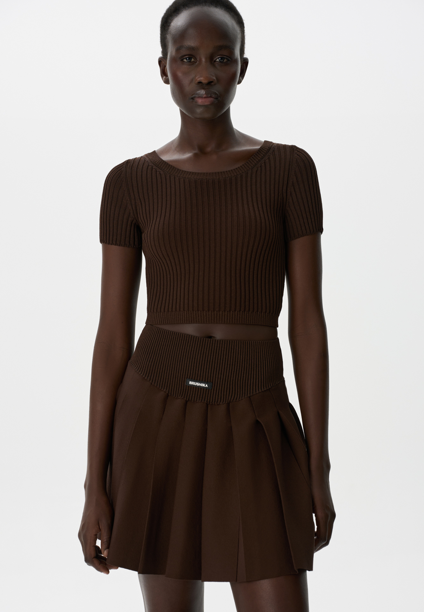 Короткий трикотажный топ из вискозы в рубчик. Модель приталенного силуэта с короткими рукавами и круглым вырезом горловины. Дополнить образ можно юбкой плиссе.