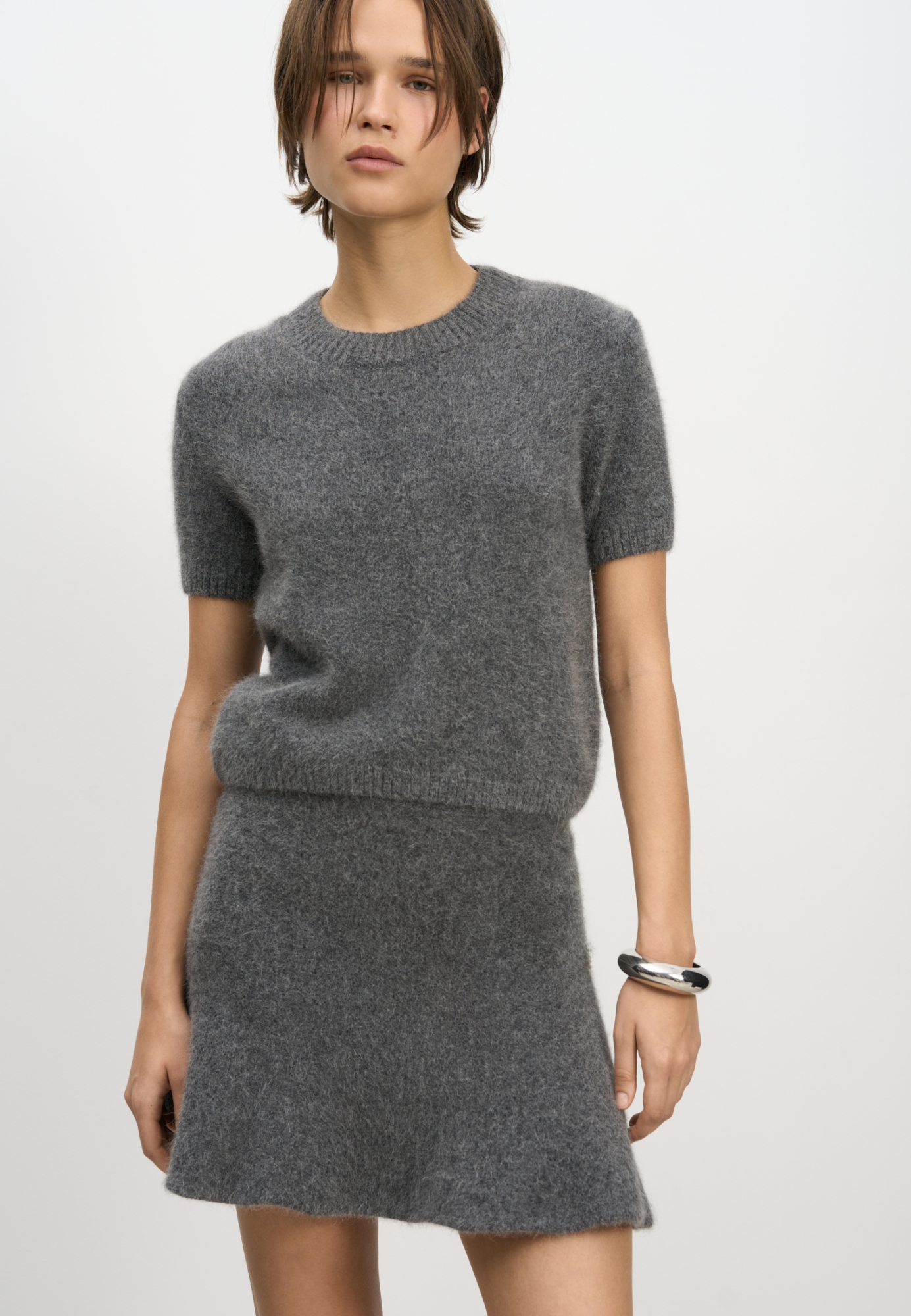 Трикотажная футболка из пуха лисы. Модель свободного силуэта, с коротким рукавом и круглым вырезом горловины. Края изделия выполнены в рубчик. Дополнить образ можно юбкой.