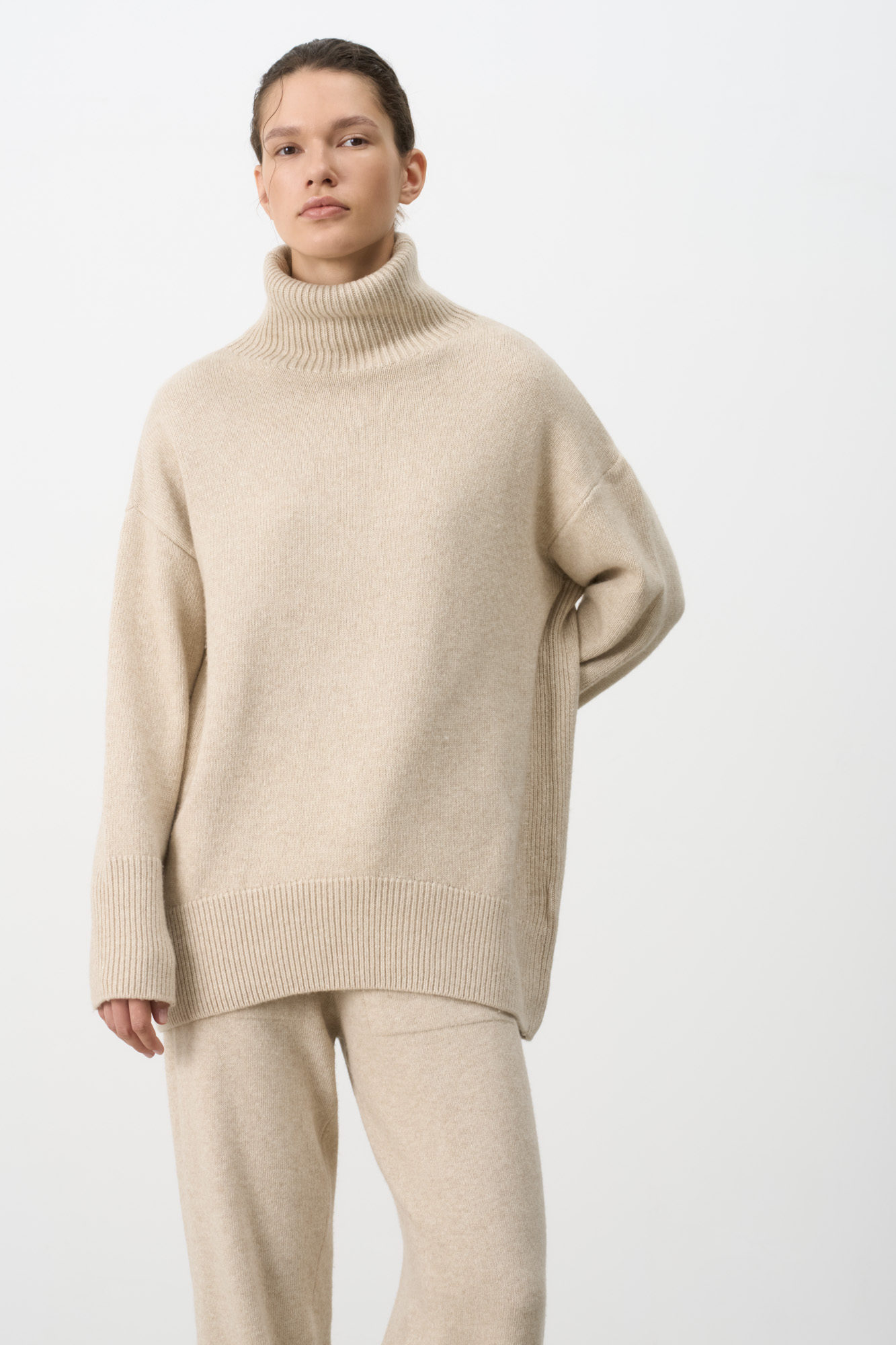 Трикотажный джемпер из мягкой шерсти с добавлением кашемира. Высокий ворот, заниженная линия плеч, удлиненная спинка. Края изделия сделаны в широкий рубчик. Можно дополнить комплектными брюками.