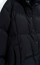 Длинный стеганый пуговик с капюшоном на кулиске. Модель свободного силуэта, с воротником-стойкой, трикотажными манжетами и боковыми карманами. Застежка на молнию под планкой с брендированными пуговицами.
