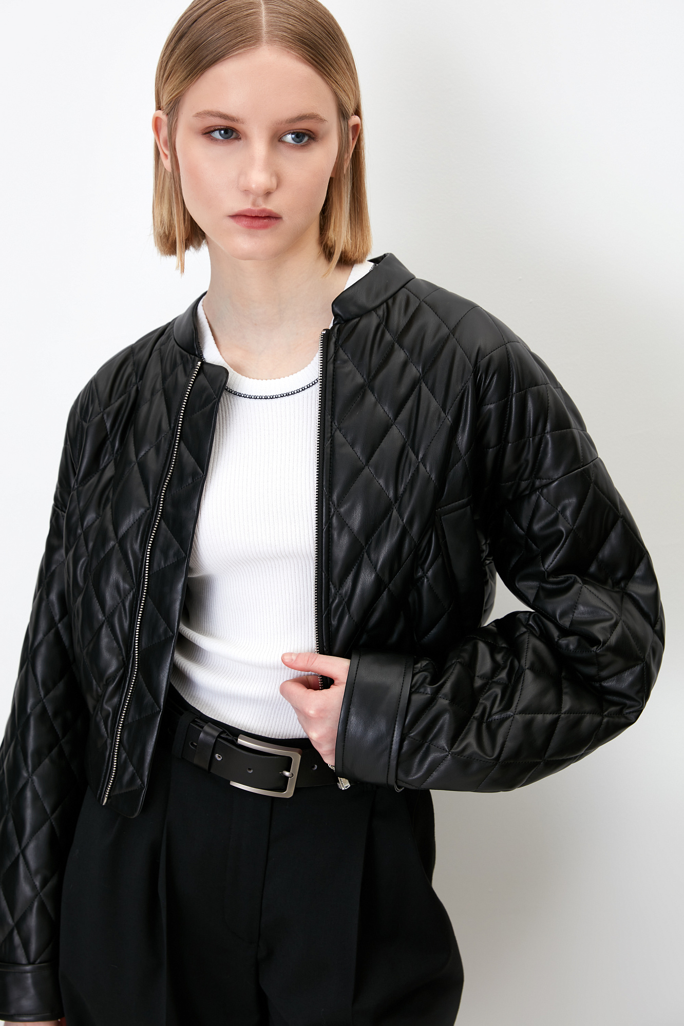 Укороченный стеганый бомбер из экокожи с воротником стойкой. Длинные рукава с манжетами на кнопках. Передние боковые карманы. Эластичный широкий пояс на резинке. Застегивается на металлическую молнию.