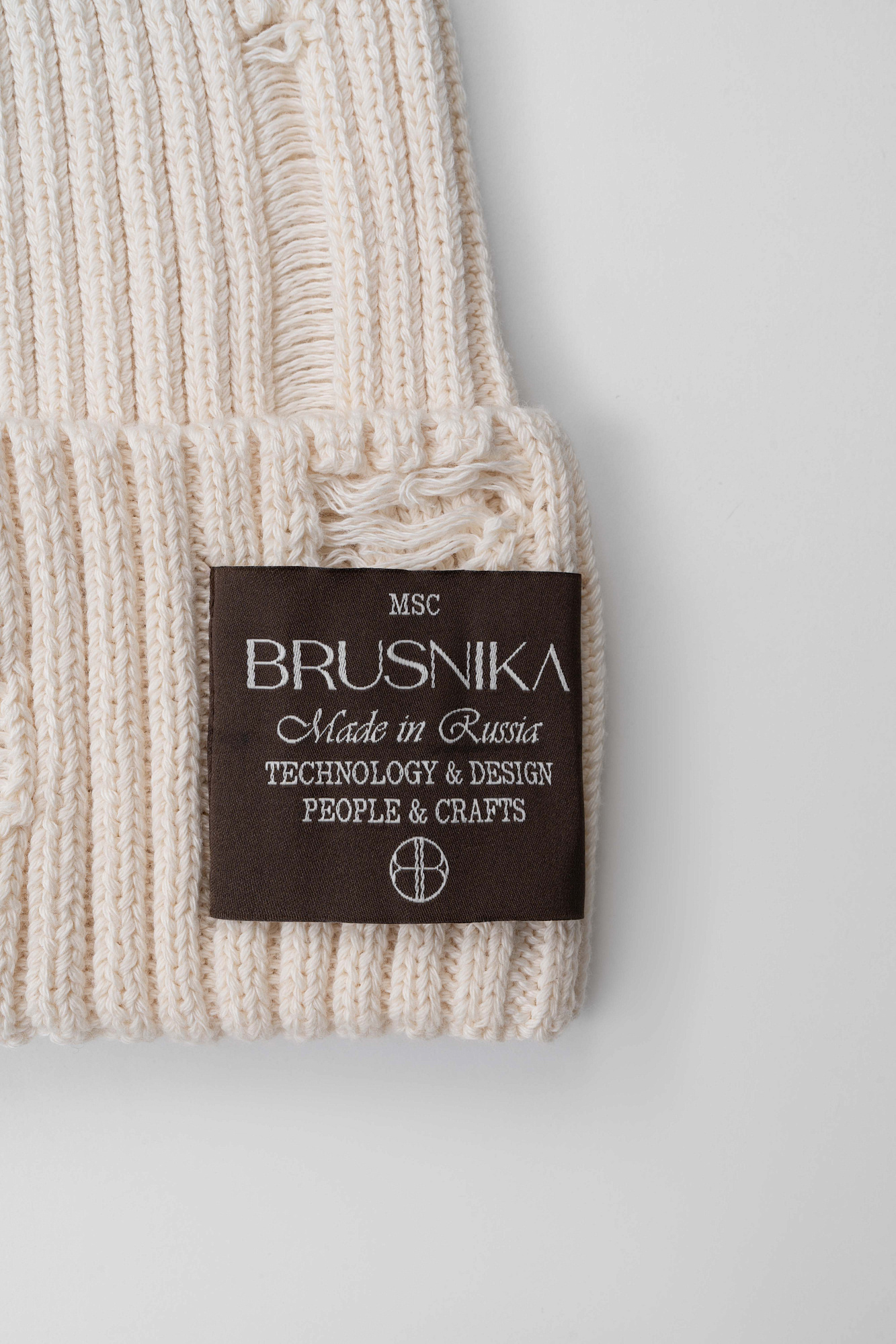 Трикотажная шапка из 100% хлопка. Модель выполнена с пропуском петель, имитируя дрань. Изделие декорировано брендированным ярлыком на отвороте.