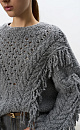 Трикотажный джемпер из шерсти мериноса в стиле бохо. Модель свободного силуэта со спущенной линией плеча и круглым вырезом горловины. Изделие декорировано вывязанными крупными косами и длинной бахромой. 
