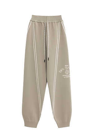 бежевый Трикотажные джоггеры из вискозы. Модель свободного силуэта, с широким эластичным поясом на кулиске, боковыми и задними карманами. Изделие декорировано брендированным жаккардом и лампасами контрастного цвета.