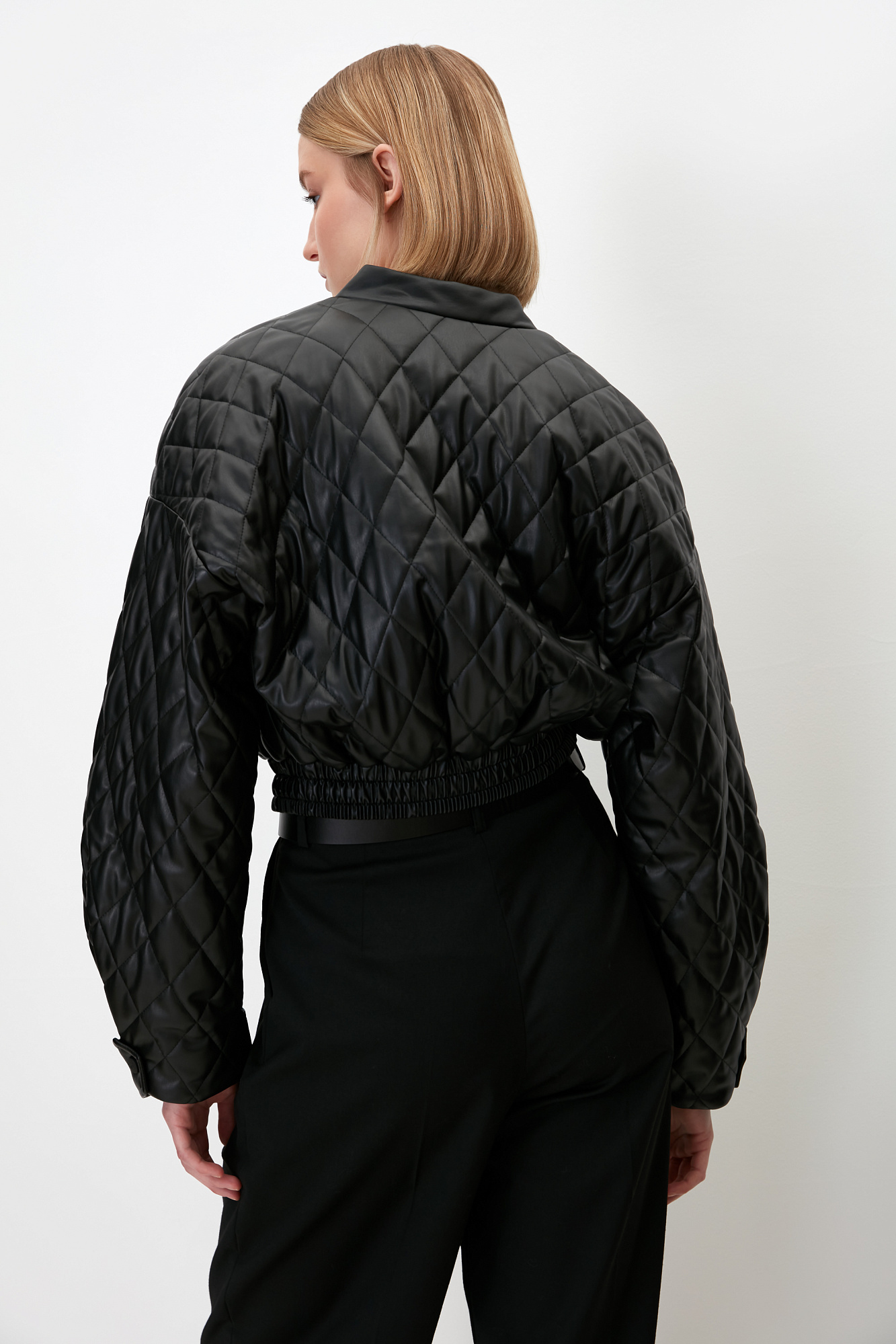 Укороченный стеганый бомбер из экокожи с воротником стойкой. Длинные рукава с манжетами на кнопках. Передние боковые карманы. Эластичный широкий пояс на резинке. Застегивается на металлическую молнию.