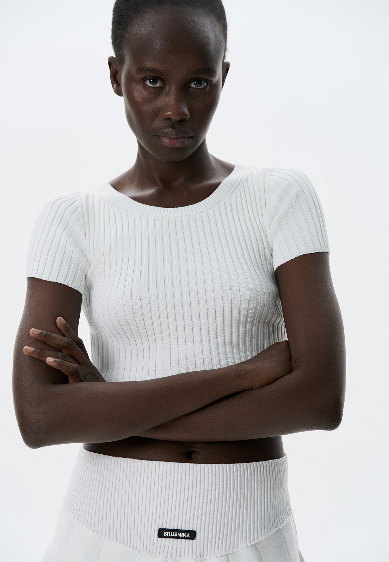 Короткий трикотажный топ из вискозы в рубчик. Модель приталенного силуэта с короткими рукавами и круглым вырезом горловины. Дополнить образ можно юбкой плиссе.