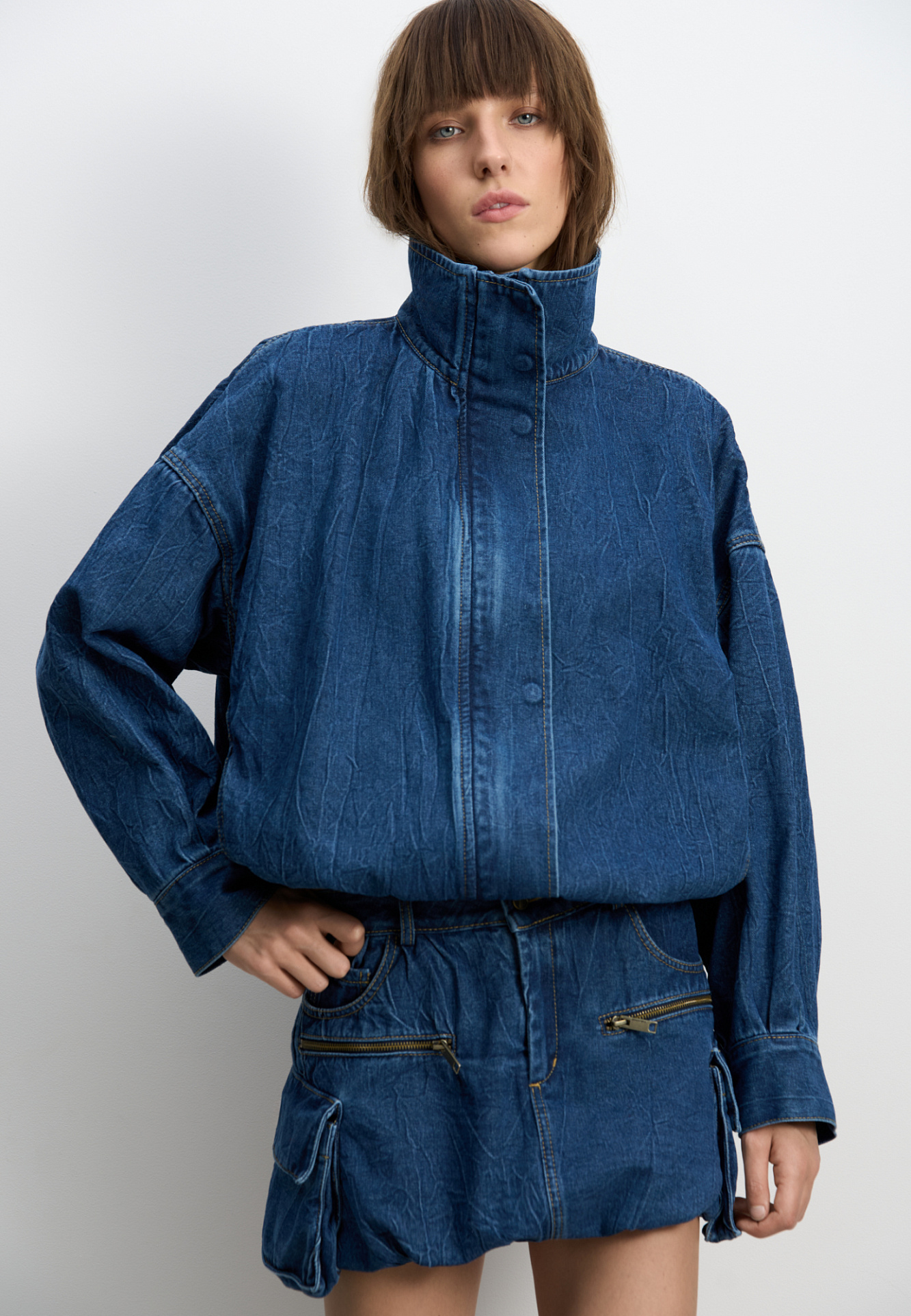 Джинсовая мини-юбка баллон из 100% хлопка. Модель с большими накладными карманами с клапанами по бокам, врезными карманами, шлевками на поясе для ремня и застежкой на молнию и пуговицу.