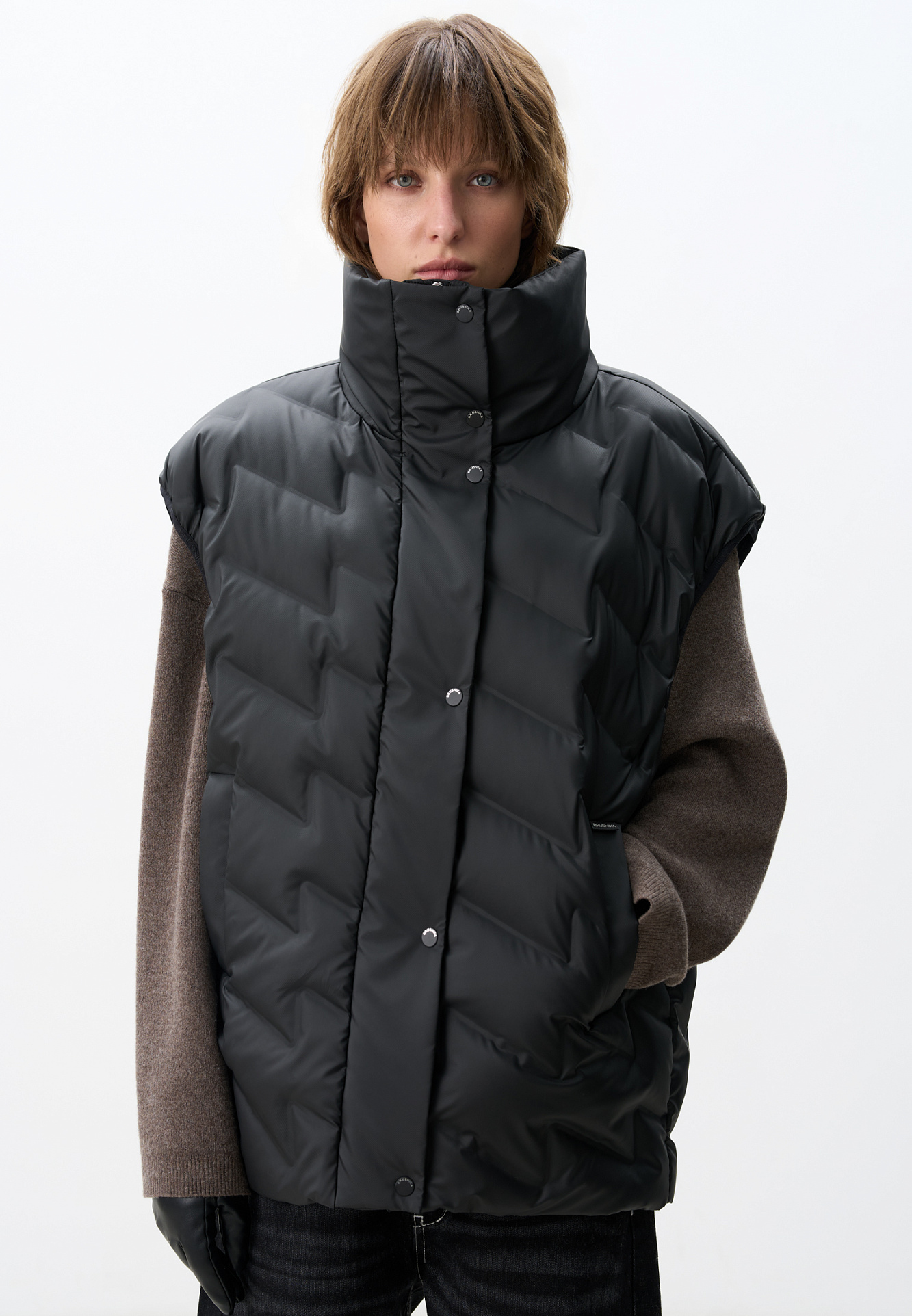 Объемный стеганый жилет на пуху. Модель прямого кроя, с воротником стойкой и боковыми карманами. Застежка на молнию и кнопки под планкой.